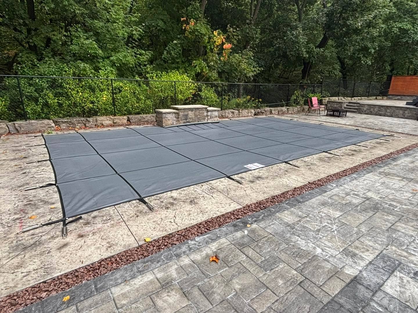 Pool closed for winter with a safety cover on a stamped concrete deck