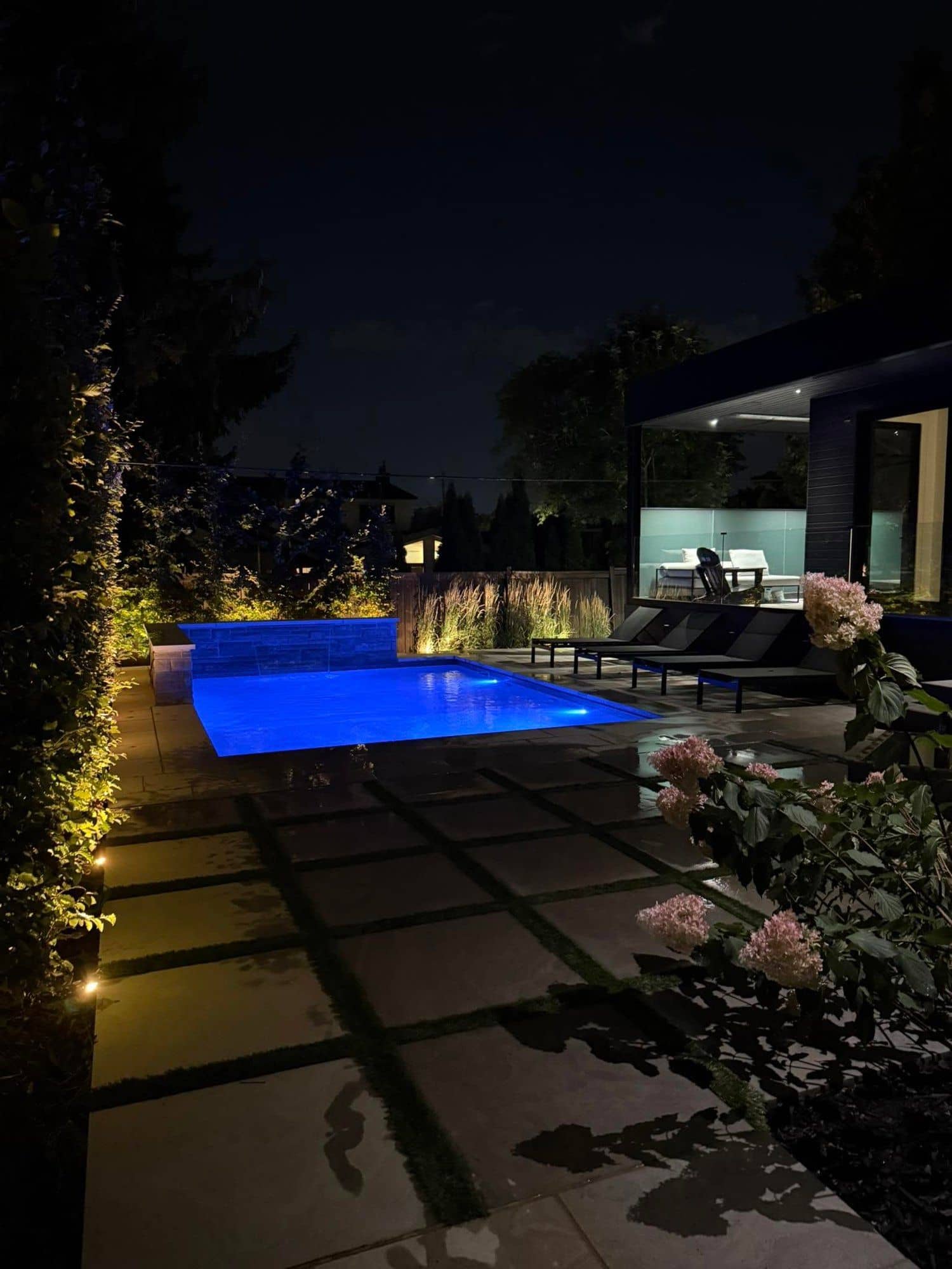 Custom inground pool lit blue at night beside a modern cabana